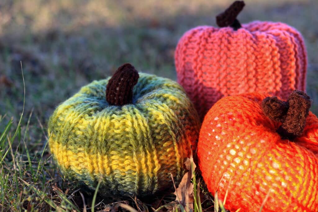 Three handmade knitted pumpkins (orange, red and green) on the grass in park